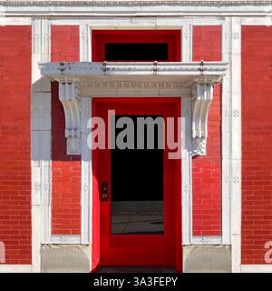 La porte rouge est située dans une façade en brique rouge, encadrée par d'élégants détails en pierre blanche et un surplomb finement sculpté et des corbeaux décoratifs, Banque D'Images