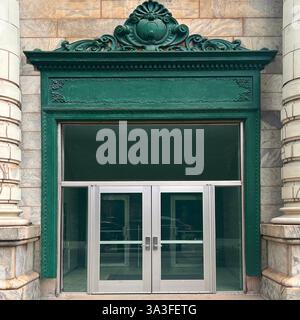 Entrée élégante aux portes en verre double argenté encadrée par une architrave en fonte verte richement décorée, située dans une façade historique en pierre. Banque D'Images