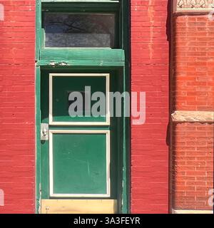 Une porte verte frappante encadrée par une façade en briques rouges audacieuse, mettant en valeur un jeu de couleurs et de textures contrastées, dans un cadre urbain. Banque D'Images