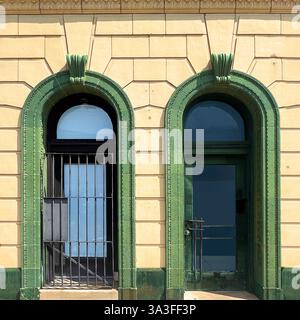 Porte et fenêtre historiques arquées encadrées de pierres vertes ornées de détails ornés, arborant des barres de sécurité en métal, placées contre une façade en pierre jaune. Banque D'Images