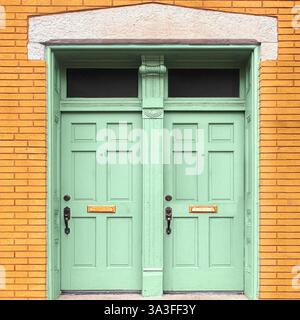 Élégantes portes doubles vert menthe avec moulures complexes, encadrées par une façade en briques jaunes chaudes et une arche décorative en calcaire. Banque D'Images