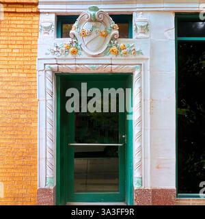Une entrée de bâtiment historique avec des détails en terre cuite vitrée, avec une crête décorative avec des ornements floraux au-dessus d'une porte en verre vert. Banque D'Images