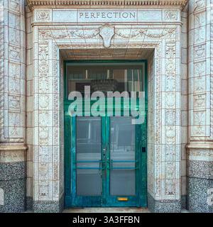 Une double porte verte ornée avec une patine altérée, située dans une façade en pierre finement sculptée étiquetée « PERFECTION », à Chicago Banque D'Images