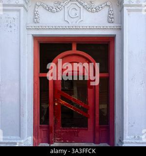 Une porte arquée rouge vintage, située dans une façade blanche ornée de détails architecturaux et d'un emblème décoratif « G » à Chicago. Banque D'Images