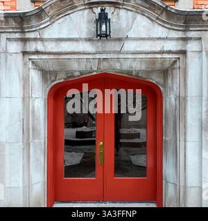 Portes doubles rouges de style gothique avec panneaux de verre cintrés dans une entrée en pierre altérée. Banque D'Images