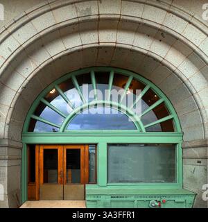 Grande entrée voûtée avec encadrement en métal vert menthe et portes doubles en bois dans une façade historique en pierre Banque D'Images