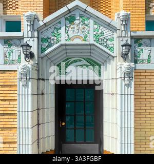 Entrée art déco ornée de détails en terre cuite ornés de motifs floraux et animaux, de touches décoratives vertes et dorées et d'une façade classique en briques. Banque D'Images