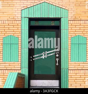 Porte Art déco dotée d'une porte en verre élégante encadrée de carreaux de céramique vert menthe et de briques décoratives. Banque D'Images
