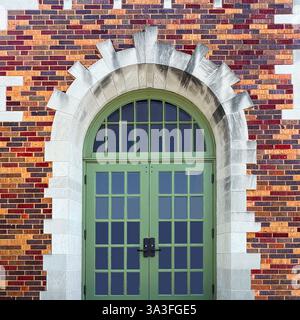 Portes vertes arquées avec panneaux de verre, situées dans une grande entrée en pierre arquée, entourées de briques colorées et détaillées. Banque D'Images