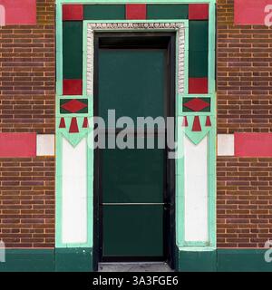 Porte urbaine Art déco avec porte vitrée encadrée de motifs géométriques vibrants en vert, menthe, rouge et blanc, entourée de briques. Banque D'Images