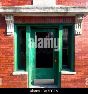 Porte verte vintage avec panneau de verre, encadrée par des pierres détaillées et façade en briques vitrées rouges. Banque D'Images