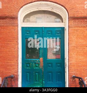 Portes doubles sarcelle vieillies avec panneaux de verre et fenêtre à tableau arrière cintré dans une façade historique en brique orange aux détails ornés à Chicago. Banque D'Images