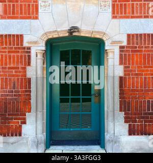 Porte vitrée verte située dans une arche en pierre de style gothique ornée de sculptures complexes, encadrée par une façade en brique orange à Chicago. Banque D'Images