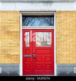 Portes doubles rouges avec panneaux de verre et fenêtre de tableau arrière dans une façade en brique jaune avec garniture décorative à Chicago. Banque D'Images