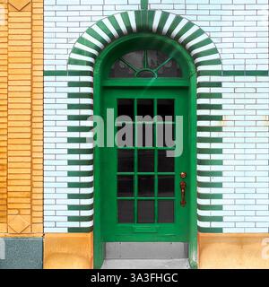 Porte verte avec vitres sertie dans une arche carrelée blanche et verte frappante, brique vitrée blanche à Chicago. Banque D'Images