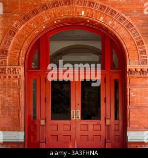 Une grande double porte rouge dans une entrée en brique voûtée, ornée de détails en terre cuite complexes à Chicago Banque D'Images
