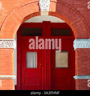 Double porte rouge encadrée par une grande entrée en brique voûtée avec des détails complexes en pierre. Banque D'Images