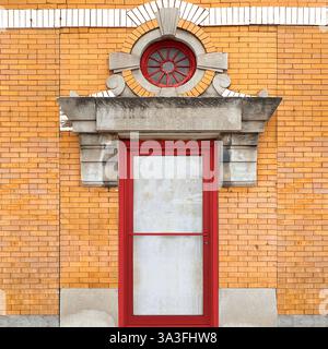 Porte rouge située dans un bâtiment historique en briques, encadrée par des détails en pierre complexes et surmontée d'une fenêtre circulaire accentuée à Chicago Banque D'Images