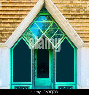 Porte verte géométrique avec vitraux sertis dans un cadre en pierre triangulaire, présentant un design architectural moderne à Kraków, en Pologne Banque D'Images