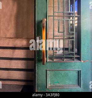 Une porte en bois vert vintage avec des ferronneries géométriques et une patine usée se trouve partiellement ouverte dans un bâtiment historique de Cracovie Banque D'Images