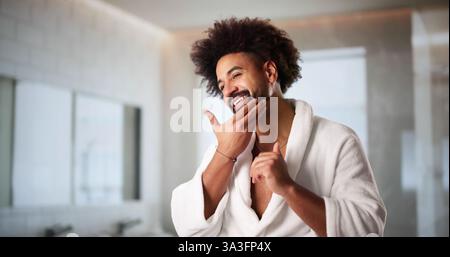 Homme afro-américain appliquant la crème faciale dans la salle de bains miroir reflet. Banque D'Images