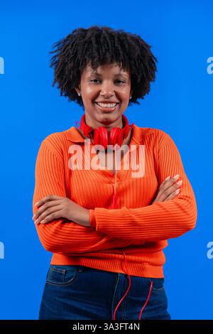 Femme afro-américaine souriante avec des écouteurs rouges posant sur fond bleu Banque D'Images
