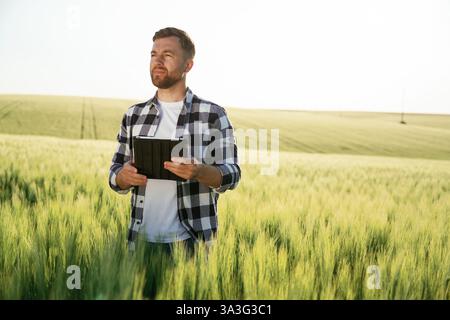 Tablette numérique entre les mains. Bel homme est sur le champ agricole pendant la journée. Banque D'Images