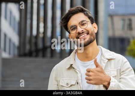 J'aime. Heureux homme indien lève les pouces vers le haut est d'accord avec quelque chose donne une réponse positive recommande la publicité aime la rétroaction de bonne idée, célébrant la victoire de succès. Arabian Guy debout dans la rue de la ville Banque D'Images