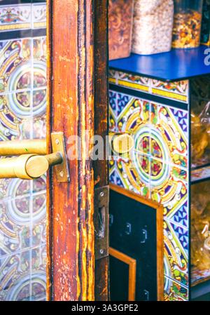 Une porte en bois vieilli avec des poignées en laiton s'ouvre pour révéler des carreaux de céramique colorés décorant l'intérieur d'une taverne espagnole traditionnelle. Banque D'Images