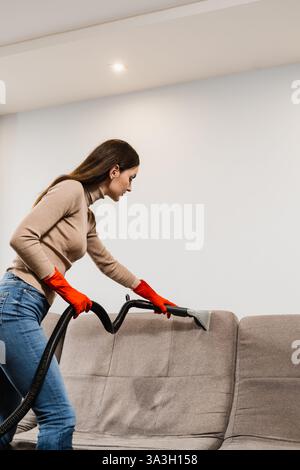 Cleaner Girl nettoie le canapé avec la machine d'extraction pour les meubles rembourrés propres à sec. Femme de ménage extrait la saleté du canapé rembourré en utilisant Banque D'Images