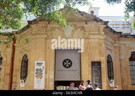 La Valette, Malte 27. Septembre 2024, les touristes entrent dans la cathédrale St John's Co par l'entrée des visiteurs, avec des affiches sur l'horloge du beffroi et le malt Banque D'Images