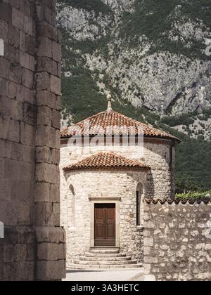 Une église crypte en pierre historique à Venzone, en Italie, avec une abside ronde et un toit en terre cuite, sur fond de montagne spectaculaire. Le site est connu fo Banque D'Images