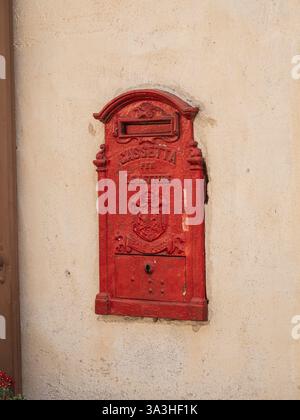 20 mai 2024 - Venzone, Italie : une vieille boîte aux lettres italienne rouge étiquetée 'Cassetta per le lettere' ('boîte aux lettres') est montée sur un mur beige altéré. Banque D'Images