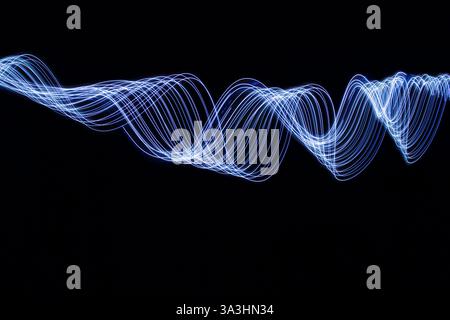 Photographie longue exposition d'une lumière bleue électrique éclatante dans des motifs tourbillonnants de mouvement sur un fond noir Banque D'Images