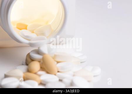 Une vue rapprochée de diverses pilules et comprimés renversés d'un contenant sur une surface blanche. Banque D'Images