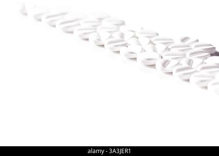 Gros plan de pilules blanches artistiquement alignées en diagonale avec une apparence propre et minimaliste sur fond blanc, mettant en évidence les concepts de santé, Banque D'Images