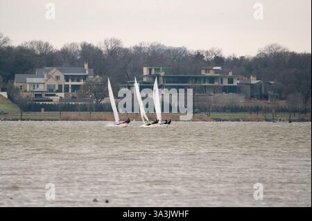 Trois petits voiliers qui traversent White Rock Lake à Dallas, Texas avec des maisons sur le rivage en arrière-plan matin d'hiver. Banque D'Images