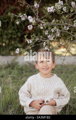 Un garçon est assis sous un amandier en fleurs, cueillant des amandes fraîches et les tenant dans ses mains. Banque D'Images