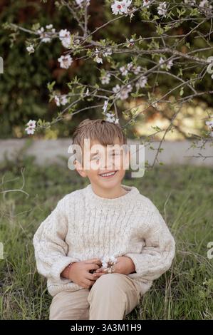 Un garçon est assis sous un amandier en fleurs, cueillant des amandes fraîches et les tenant dans ses mains. Banque D'Images