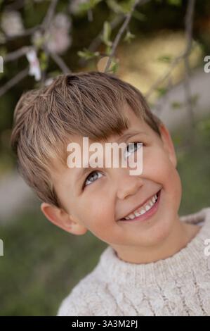Un garçon est assis sous un amandier en fleurs, cueillant des amandes fraîches et les tenant dans ses mains. Banque D'Images
