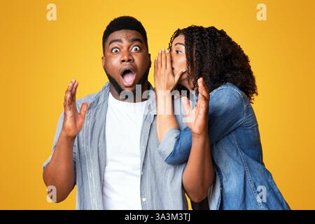Un homme réagit par surprise au secret d'une femme sur fond jaune Banque D'Images
