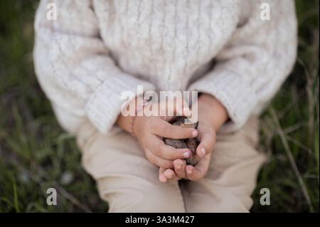 Un garçon est assis sous un amandier en fleurs, cueillant des amandes fraîches et les tenant dans ses mains. Banque D'Images