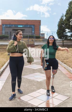 Deux amies heureuses avec des skateboards marchant dans le parc, l'une d'elles a une jambe prothétique Banque D'Images
