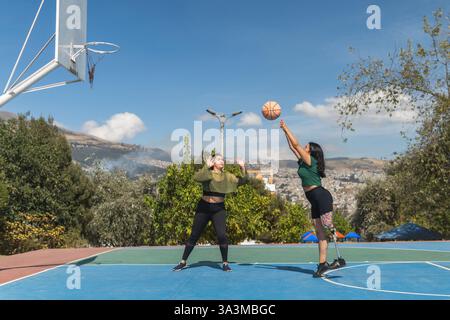 Deux jeunes femmes jouent au basketball sur un terrain extérieur, mettant en valeur la diversité, l’inclusion et l’athlétisme Banque D'Images
