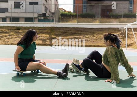 Deux jeunes femmes latines faisant une pause après avoir pratiqué le skateboard et le roller dans un parc Banque D'Images