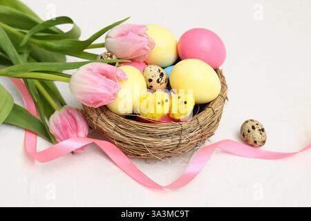 Nid avec des œufs de Pâques, des poussins et de belles fleurs de tulipe sur fond blanc Banque D'Images