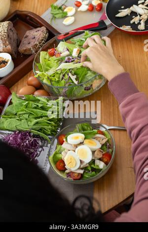 Une femme élégante appréciant une salade vibrante, assise à une table pleine de légumes frais, capturée par derrière, embrassant un repas sain et sain exp Banque D'Images