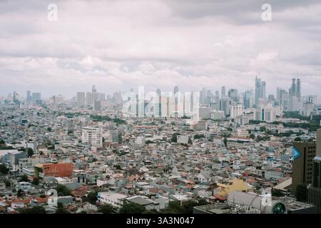 Une vue imprenable met en valeur le paysage urbain de Jakarta. Un dense groupe de maisons s'étend en dessous, contrastant avec la ligne d'horizon ponctuée par le moderne Banque D'Images