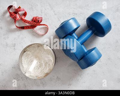 Concept de remise en forme et de perte de poids avec poudre de protéines, haltères et ruban à mesurer couché sur fond gris Banque D'Images