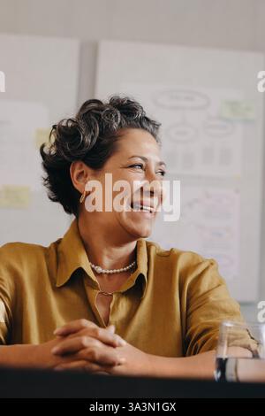 Femme professionnelle mature affichant la confiance et la positivité dans un cadre de bureau. Son comportement rayonne de succès, capturant l'essence d'un conduit Banque D'Images